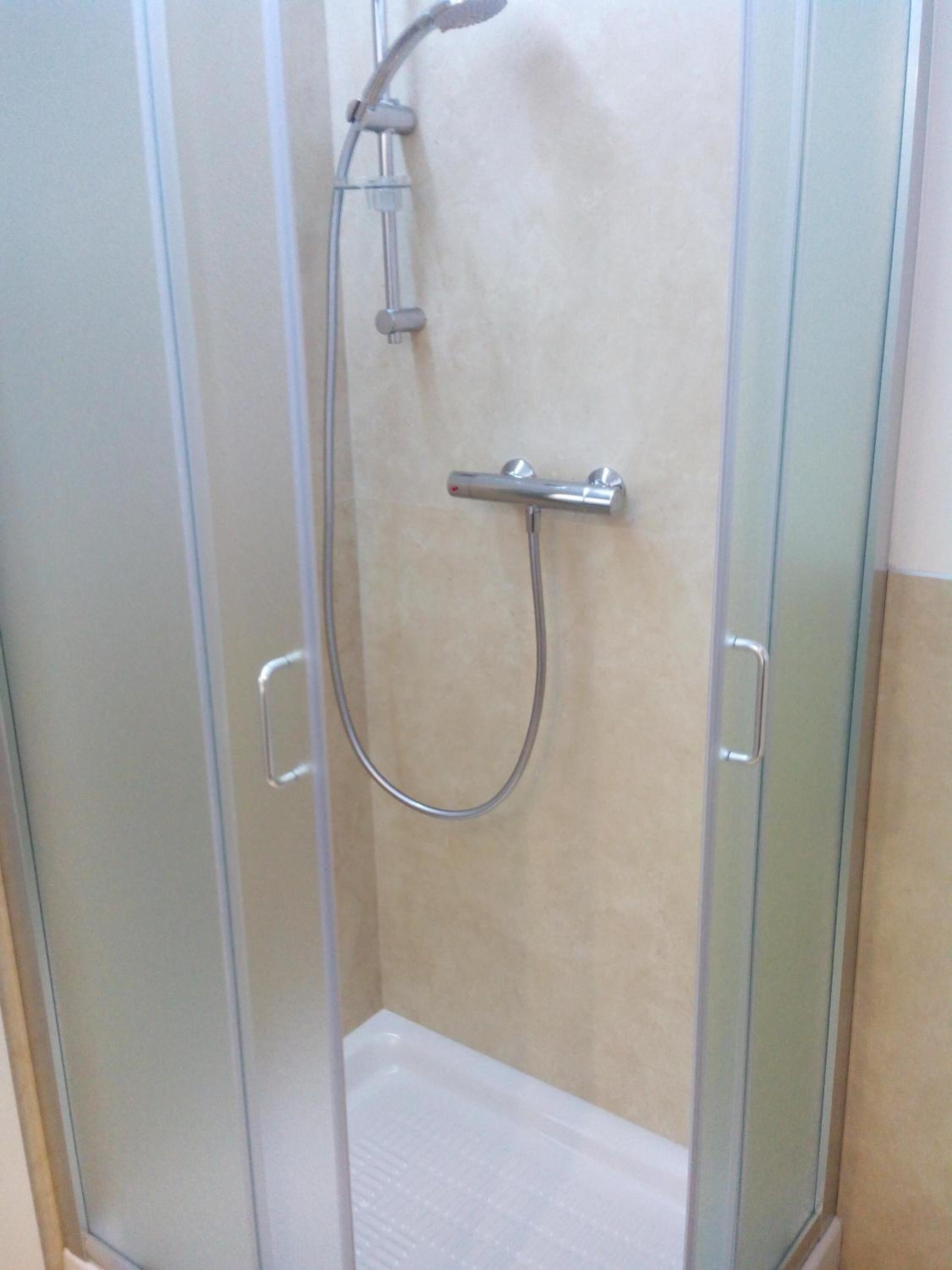 A glass-enclosed shower stall with a handheld showerhead and a wall-mounted faucet.