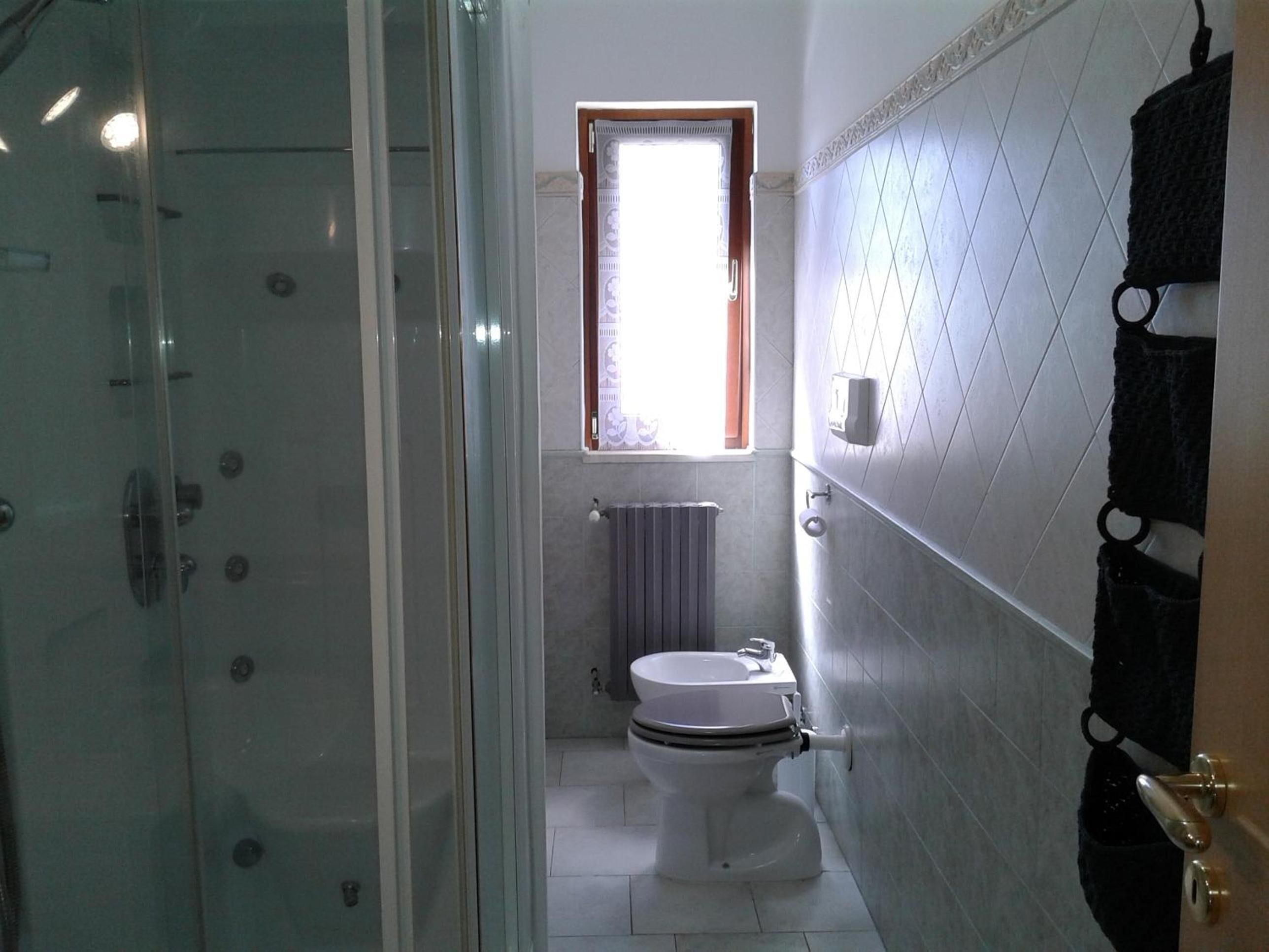 Ein Badezimmer mit Duschkabine aus Glas, Toilette und Fenster mit Blick.