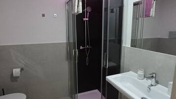 Un baño moderno con ducha envuelta en vidrio, un lavamanos blanco y un inodoro.