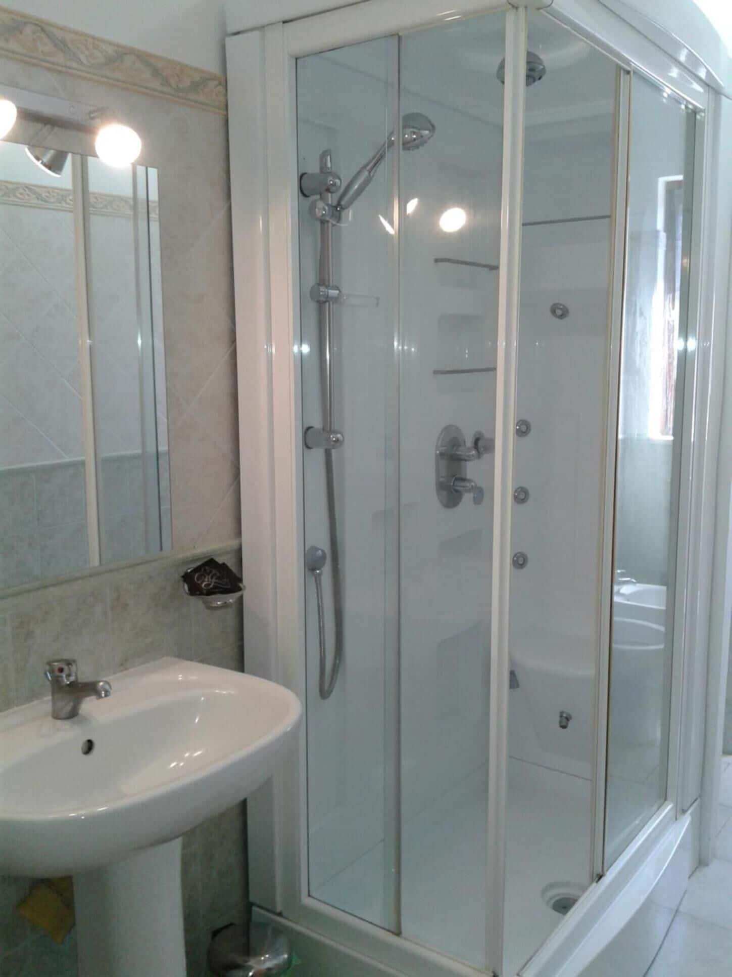 A bathroom with a glass-enclosed shower, a sink, and a mirror.