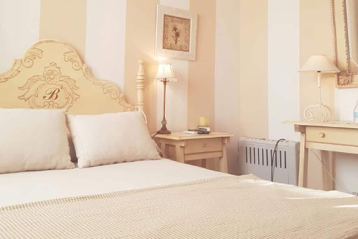 A hotel room with a bed, bedside lamp, radiator, and a framed picture on the wall.