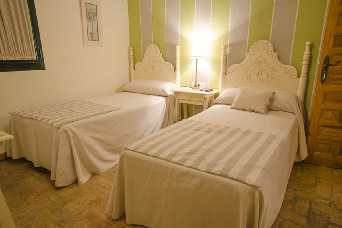 A room with two beds, each with a headboard and a bedside table with a lamp.