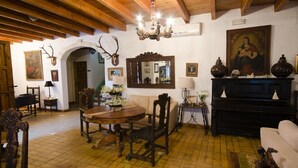 A traditional room with wooden beams, a dining table with chairs, a sofa, a piano, and a mirror on the wall. - Hotel Rural Molino la Boticaria (Marchena)