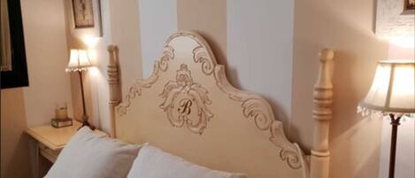 A bed with a headboard featuring a monogram, two bedside tables with lamps, and a framed picture on the wall.