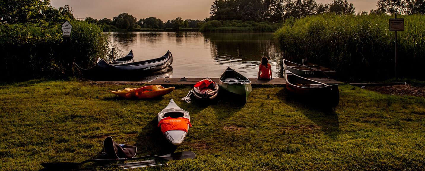 Un espacio con césped, varias kayaks y una tabla de remo cerca del agua.