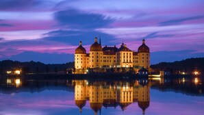 Un edificio grande e iluminado con múltiples cúpulas, reflejado en una superficie acuática tranquila.
