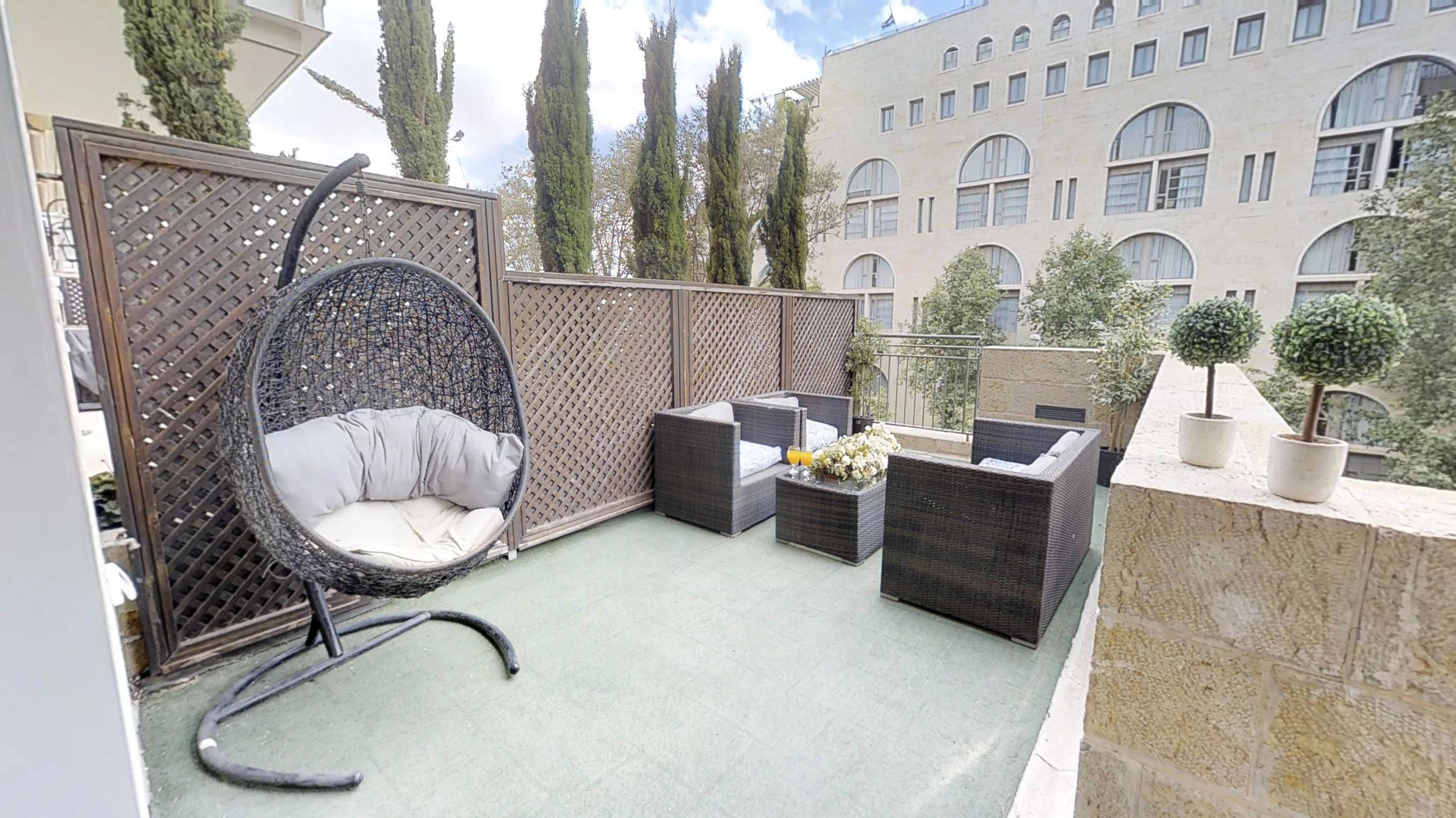Un balcon agrémenté de meubles en osier, notamment un fauteuil suspendu et deux canapés, une petite table avec des boissons et des plantes en pot.