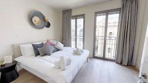 A modern hotel room with a large bed, a bedside table, and a view of the city through large windows. - Rental Israel - Mamilla Residences (Jerusalem)