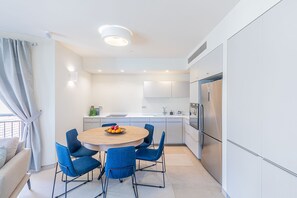 A modern kitchen with a round wooden table, blue chairs, and a stainless steel refrigerator.