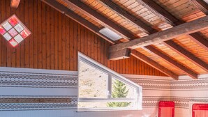 An indoor swimming pool with wooden beams, a tiled wall, and a window overlooking a landscape.