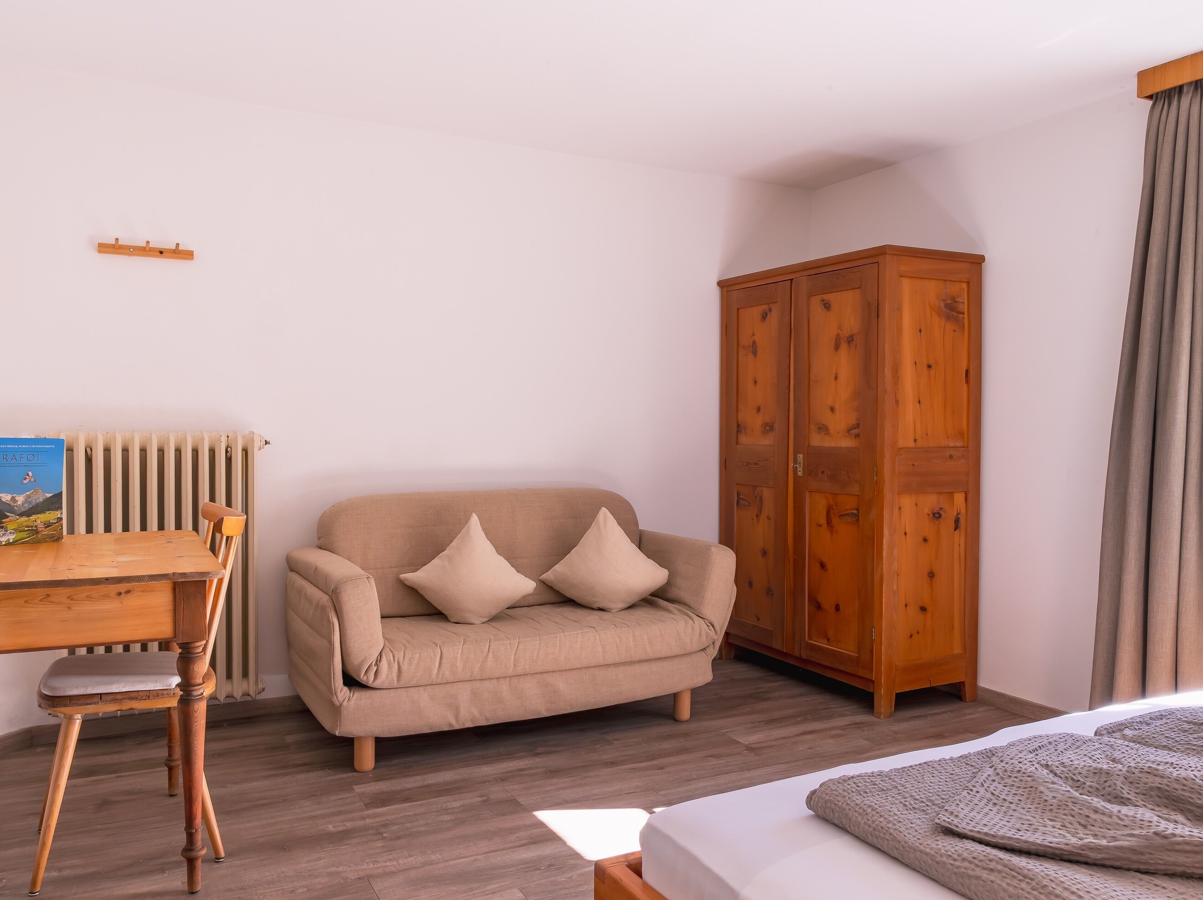 Una habitación con una silla de madera, un sofá color beige, un armario de madera y un radiador.