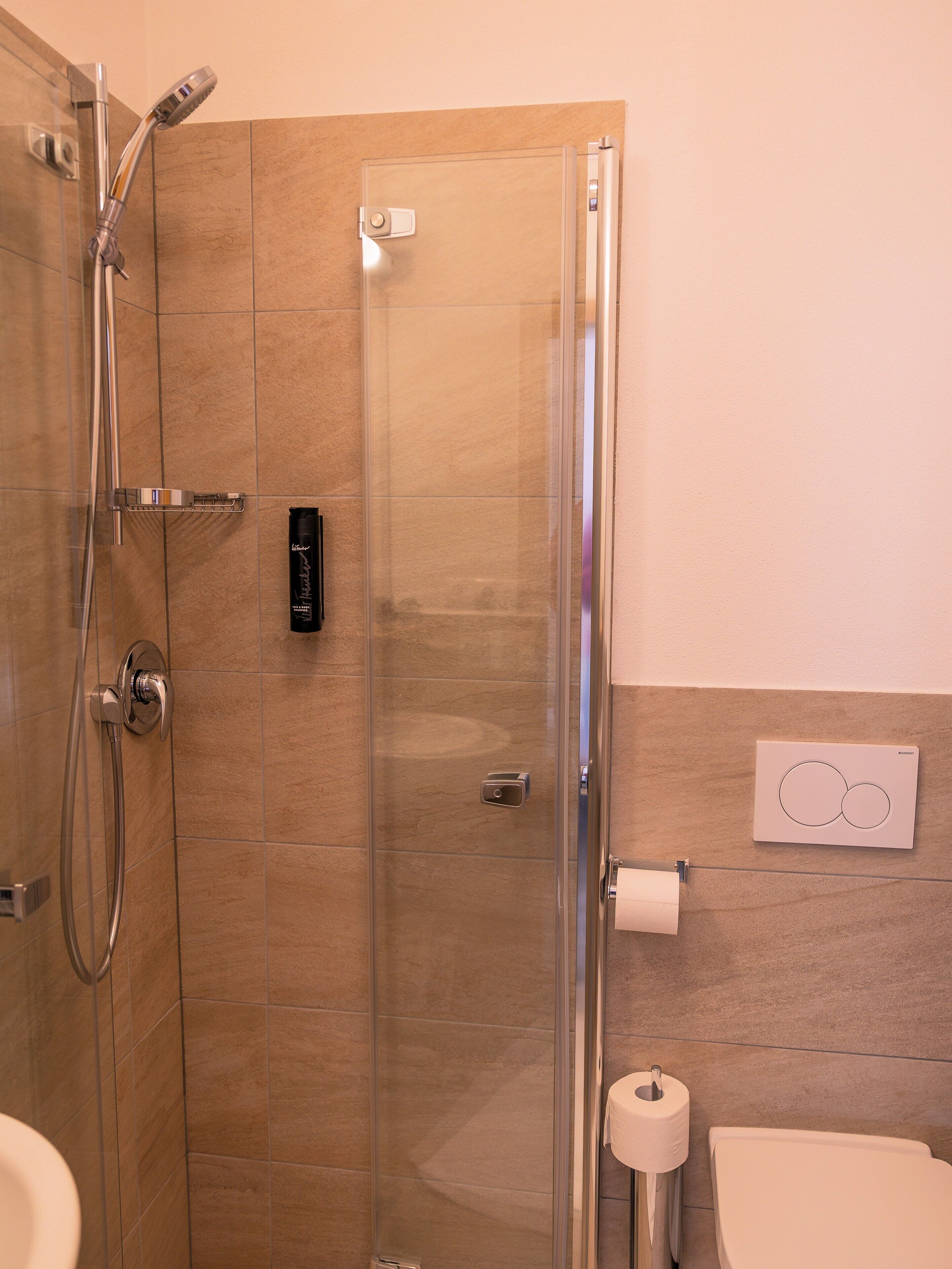 A shower with a glass door, a toilet, and a wall-mounted control panel.