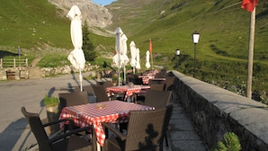 An outdoor dining area with tables and chairs, a stone wall, and a mountainous backdrop.