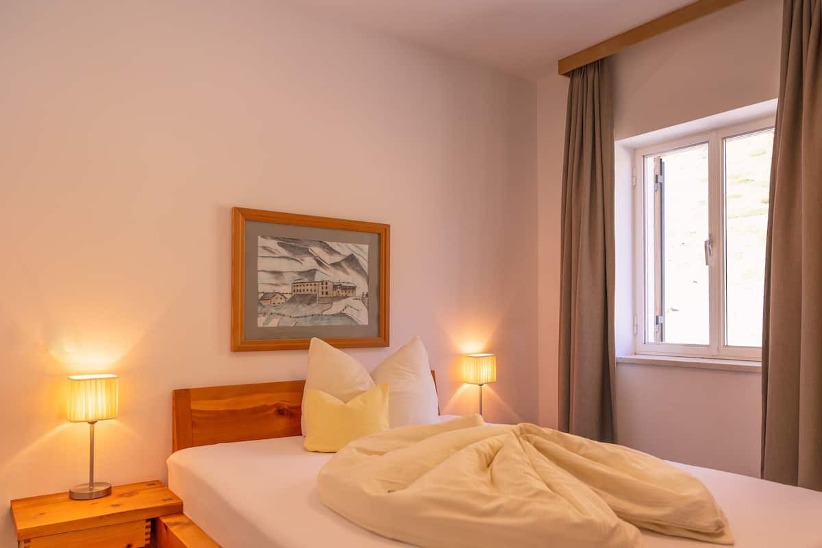 Un dormitorio con una cama, dos lámparas de noche, un cuadro en la pared y una ventana con cortinas.