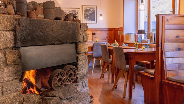 A stone fireplace with logs, a dining area with wooden furniture, and a window with a view.