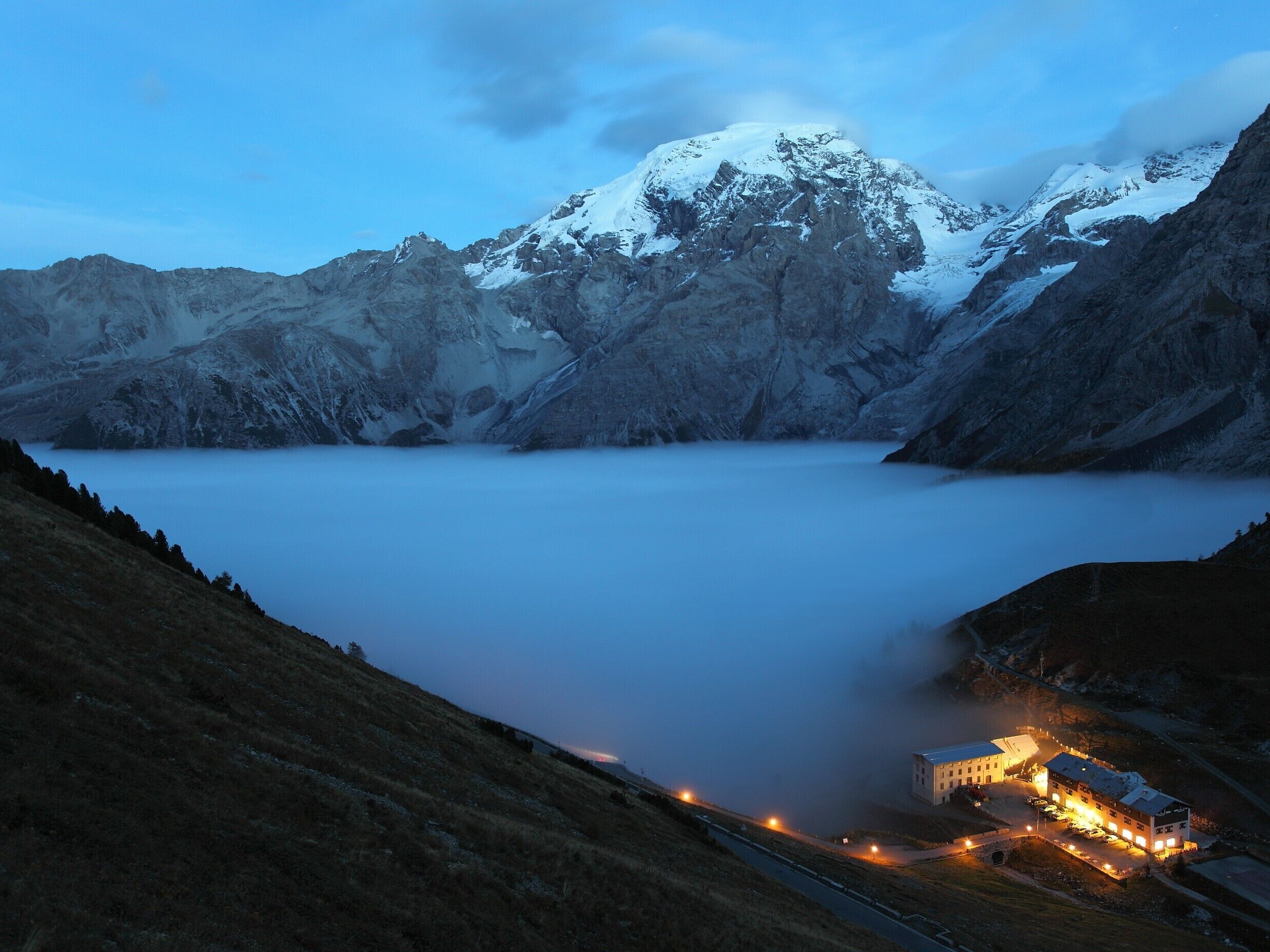 Paesaggio montuoso con un lago, un edificio con diverse stanze e una strada che conduce all'edificio.