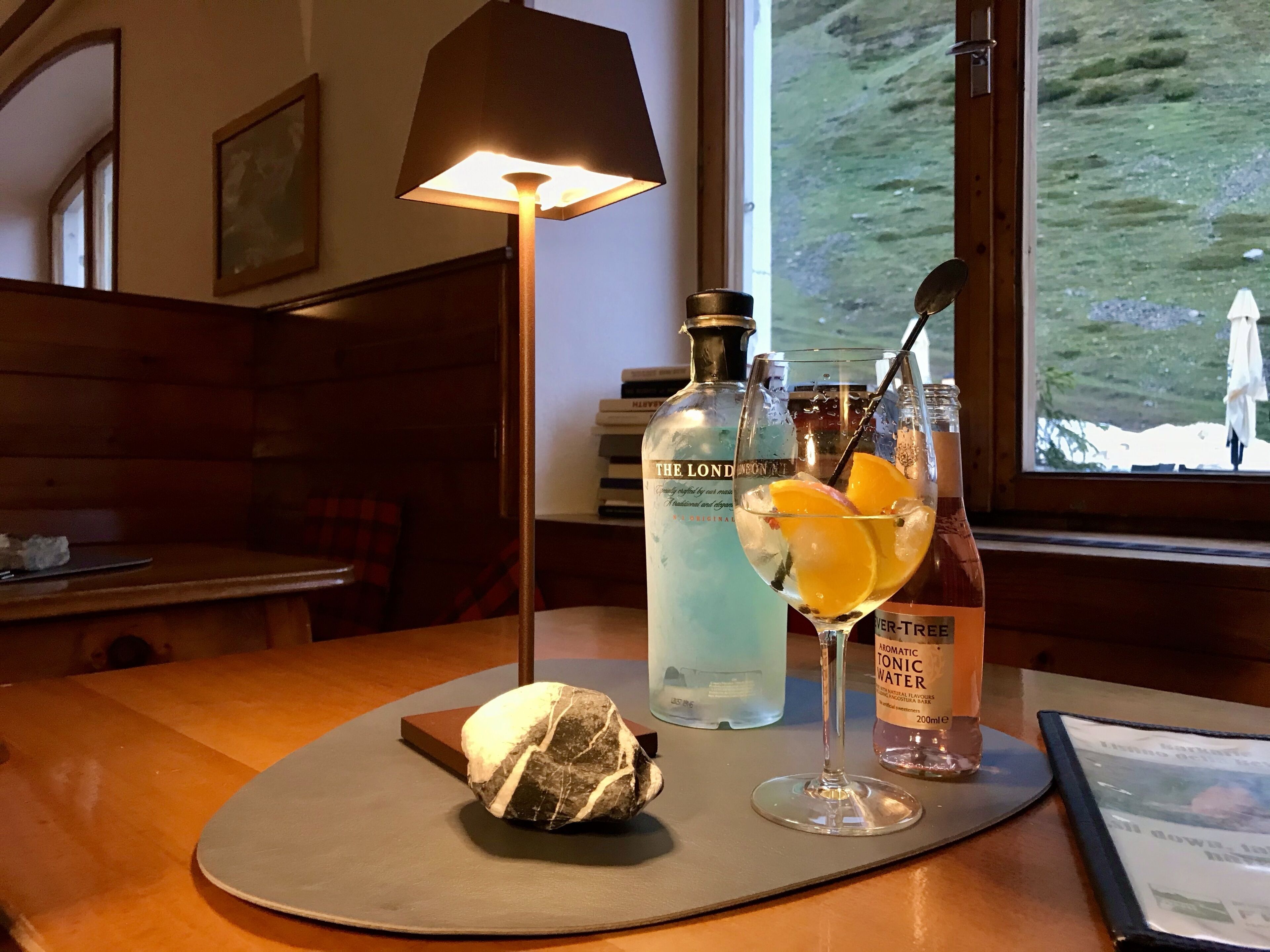 A bar area with a table, a bottle of The London Gin, a glass with an orange slice, and a bottle of aromatic tonic water.