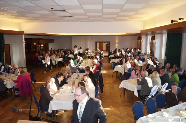 A large banquet hall with multiple round tables arranged in rows, accommodating a significant number of guests.