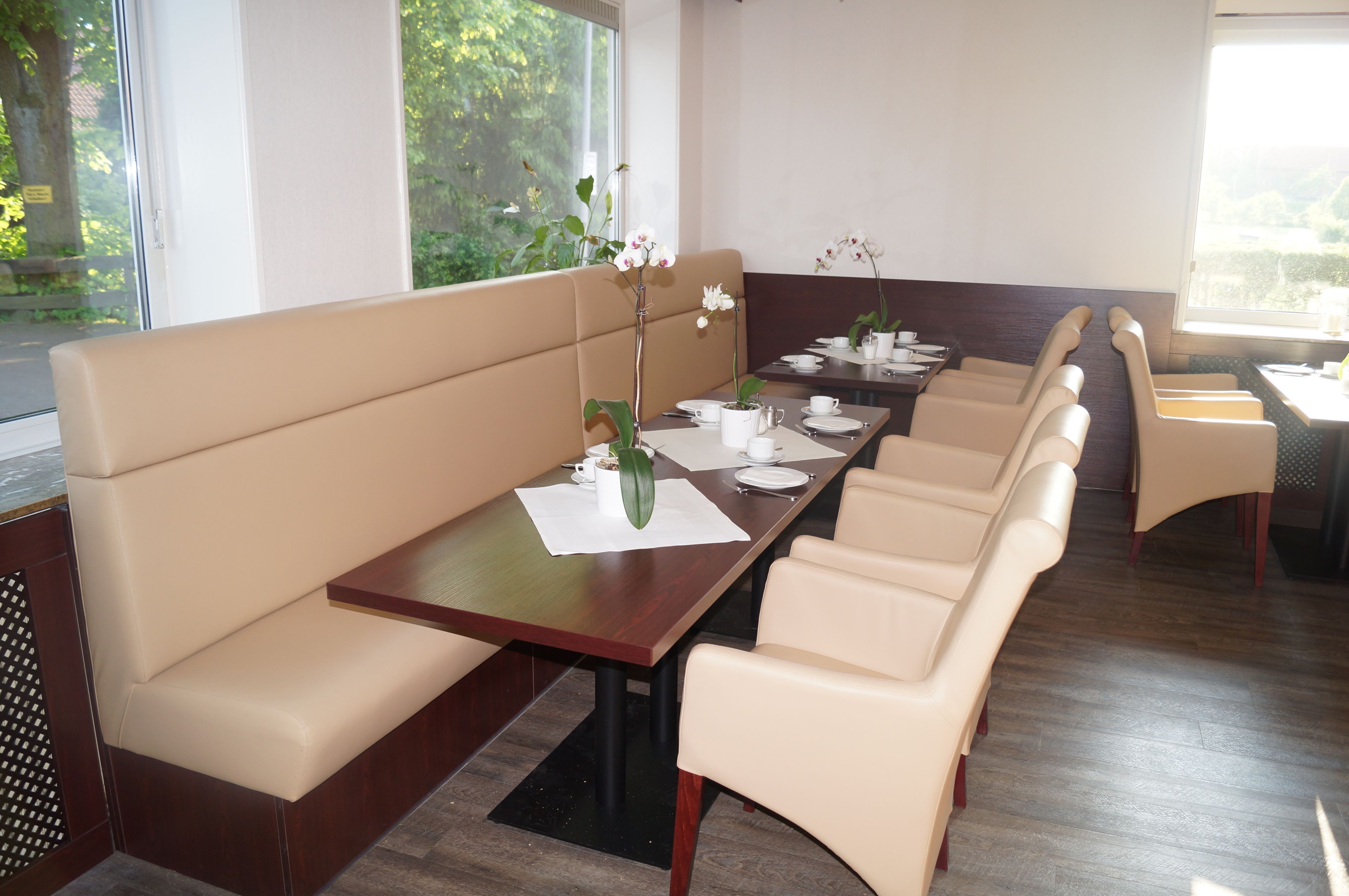 A dining area with a long table, beige cushioned seating, and a vase with white flowers.