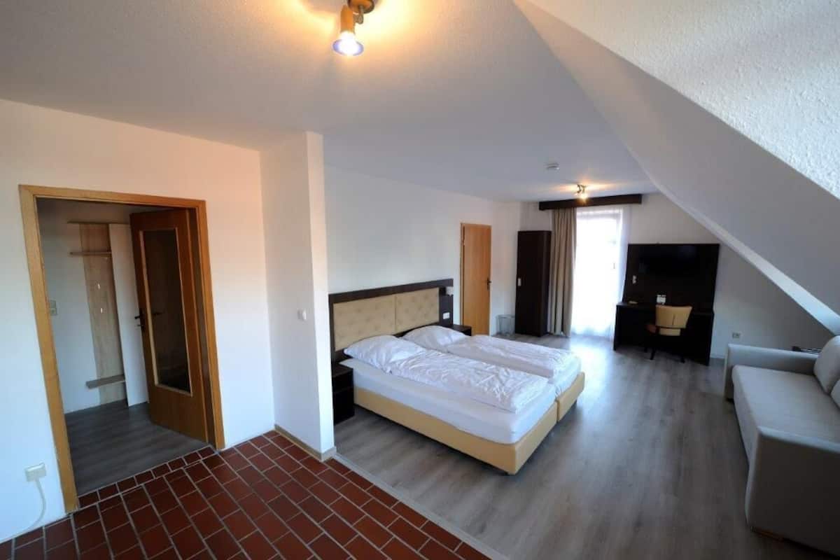 Quarto com cama, escrivaninha, cadeira e televisão.