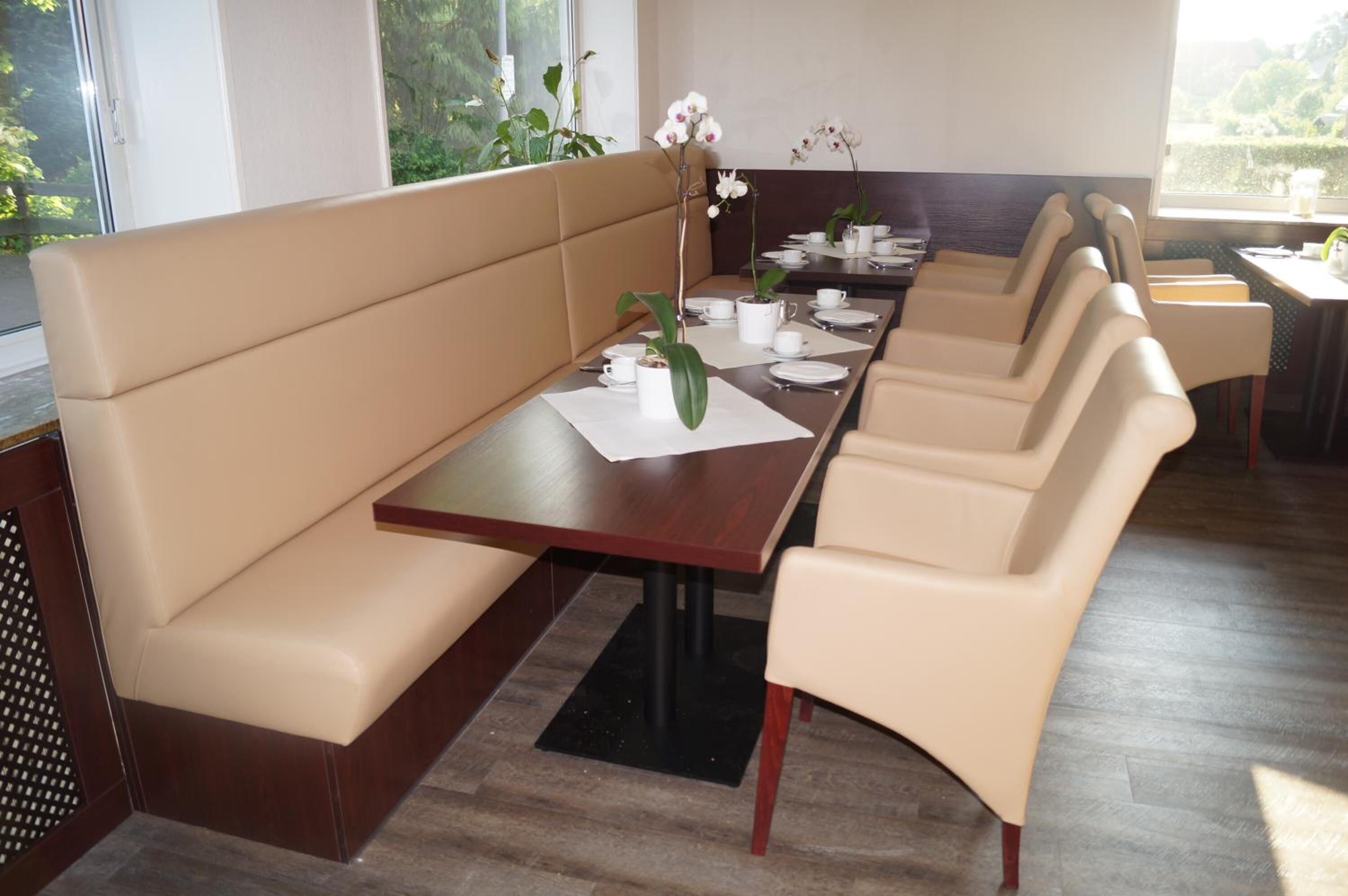Un comedor con una mesa larga, asientos con cojines color beige y orquídeas blancas.