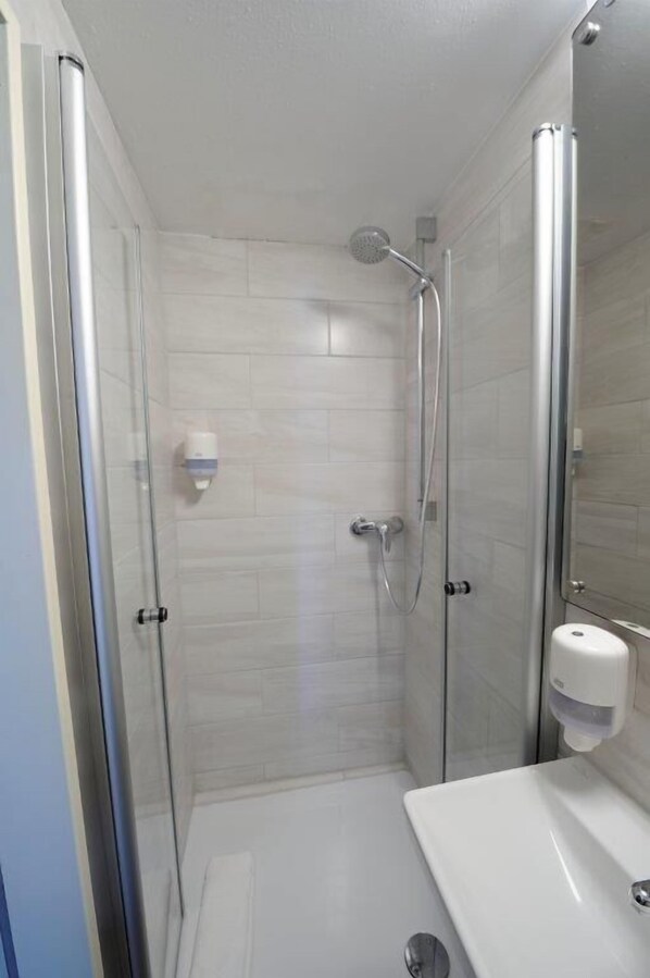 A modern bathroom with a glass-enclosed shower, a white sink, and a hand soap dispenser. - Hotel zur Post (Steimbke)