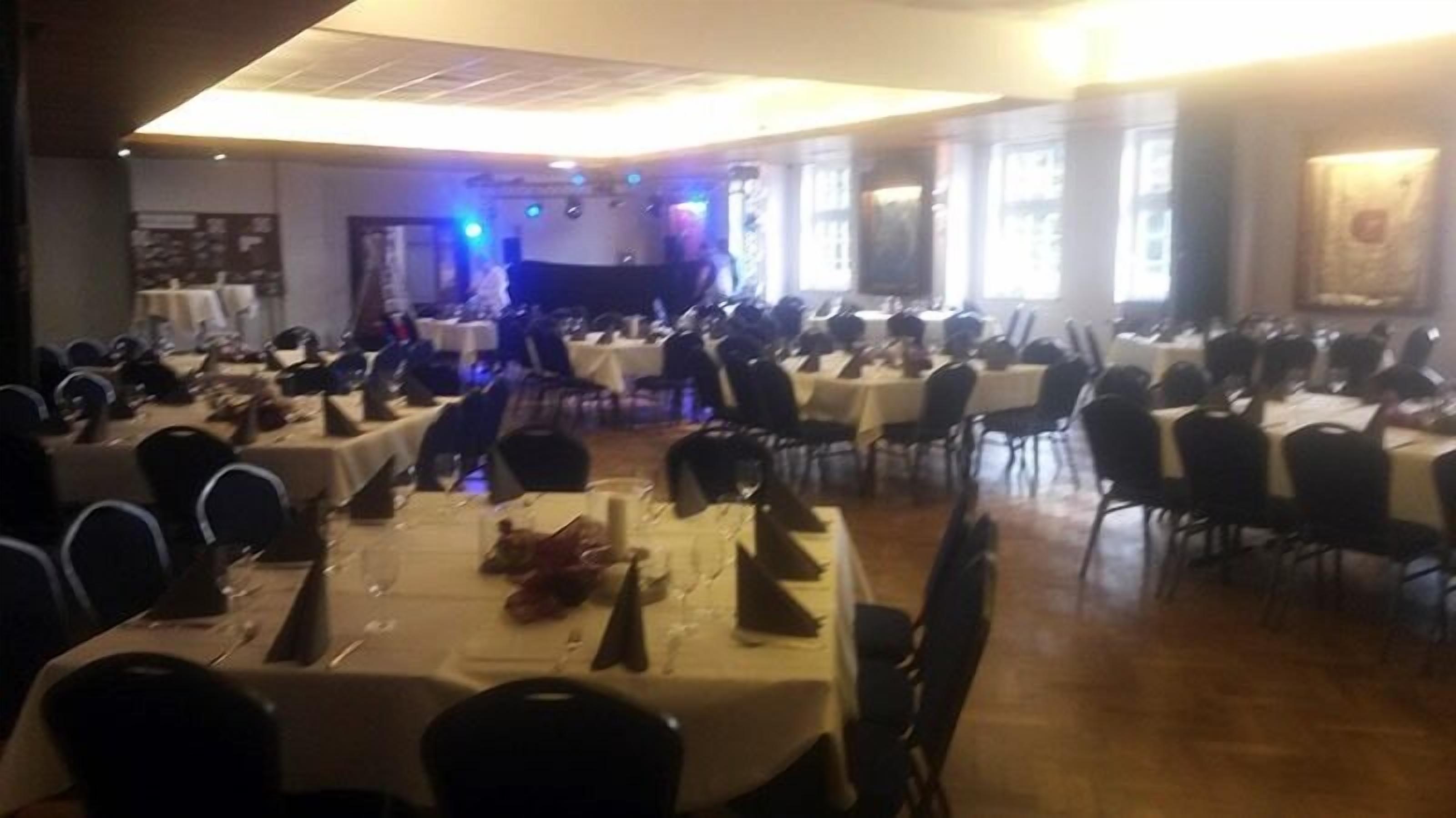 A banquet hall with multiple round tables set for dining, chairs arranged around each table, and a stage at the front.