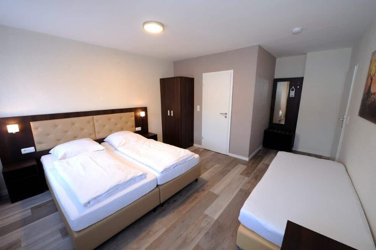 Quarto com cama de casal, uma cama individual, guarda-roupa, porta e espelho.