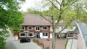 Un hôtel à deux étages, avec un toit recouvert de tuiles, une allée pavée et un arbre devant.