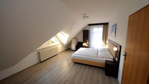 Une chambre avec un plafond en pente, un lit, une table de chevet, une fenêtre avec des rideaux et un radiateur.