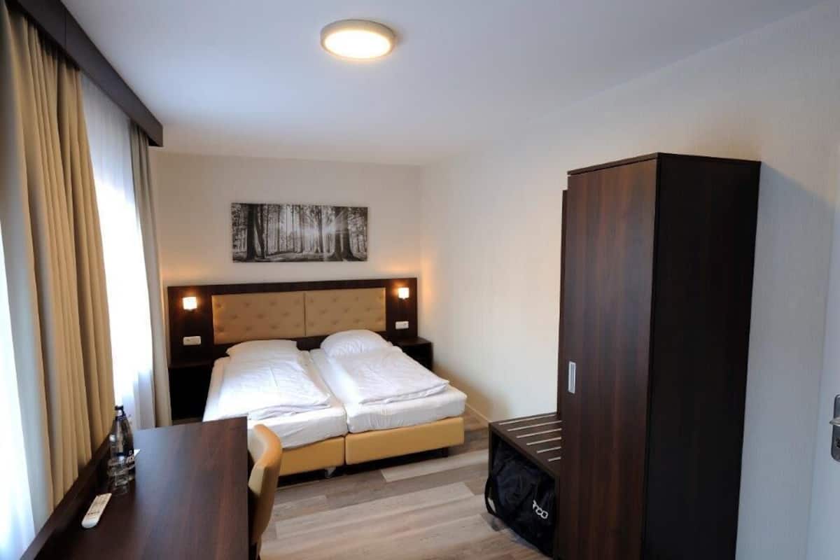 Quarto de hotel com cama, mesas de cabeceira, um guarda-roupa e um quadro na parede.
