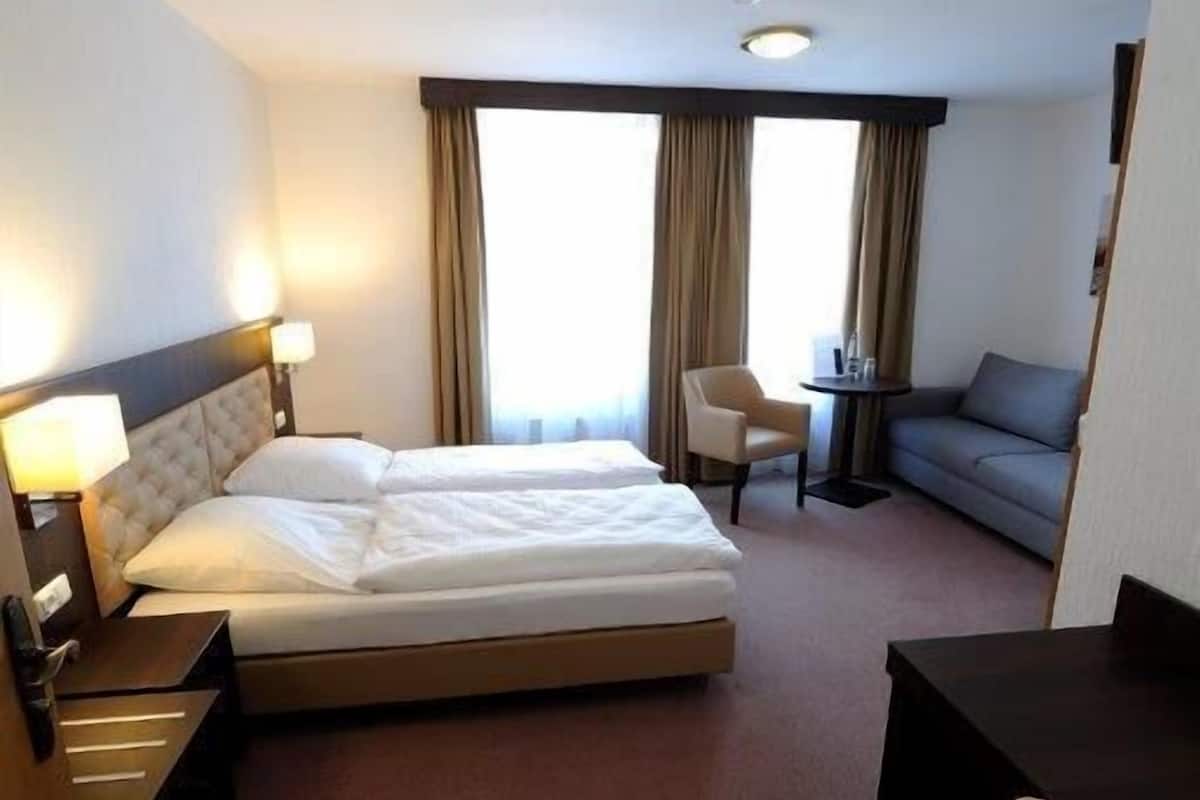 Quarto de hotel com uma cama grande, uma escrivaninha, uma cadeira e um sofá.