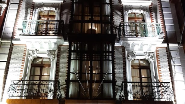 Un edificio de varios pisos con balcones ornamentados, ventanas amplias y una escalera central.