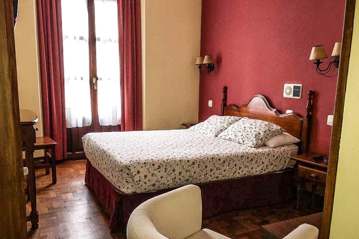 Un dormitorio con cama, una silla, un escritorio y una ventana con cortinas.