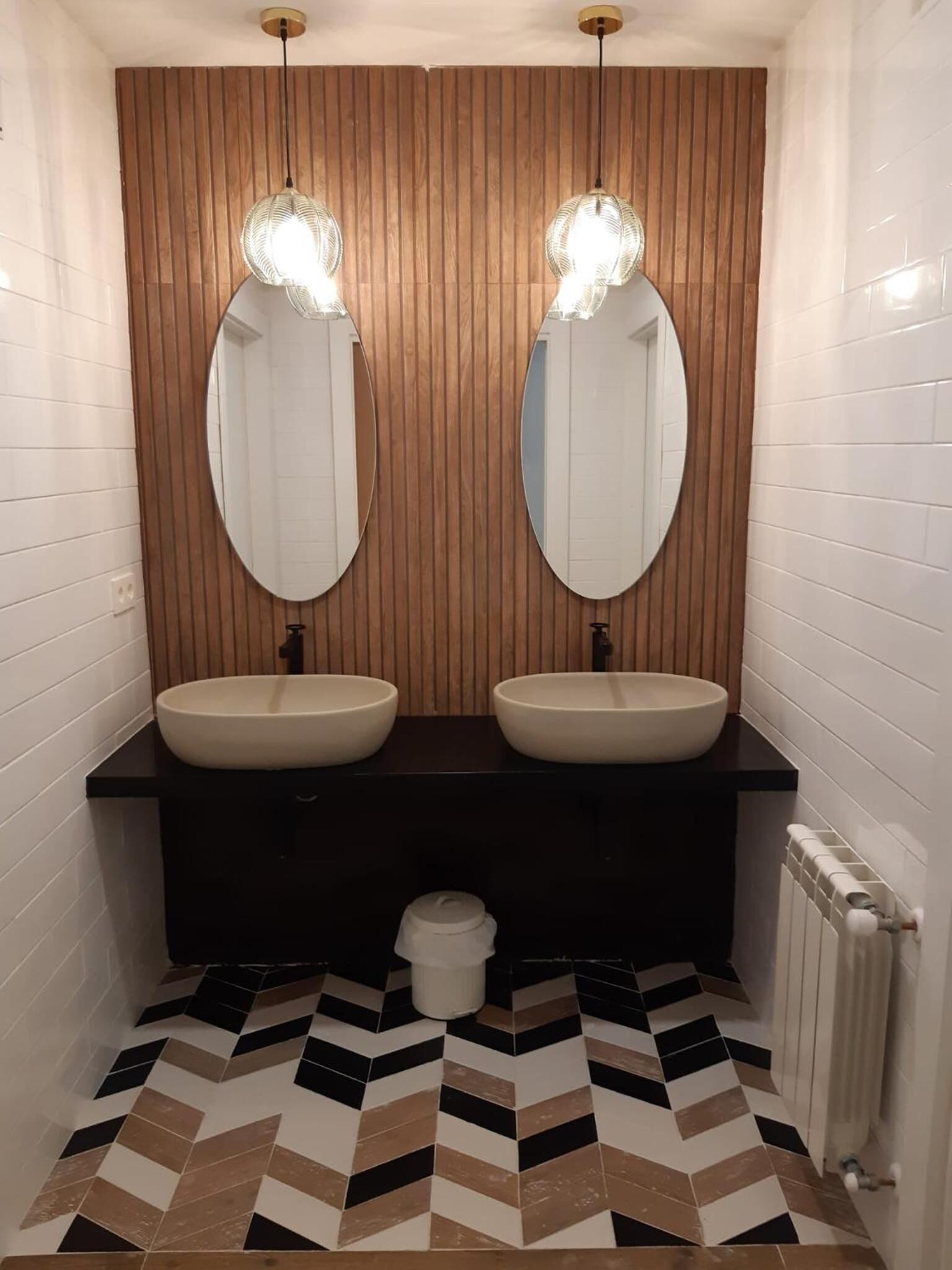 A bathroom with two sinks, wooden panel wall, and a chevron-patterned floor.