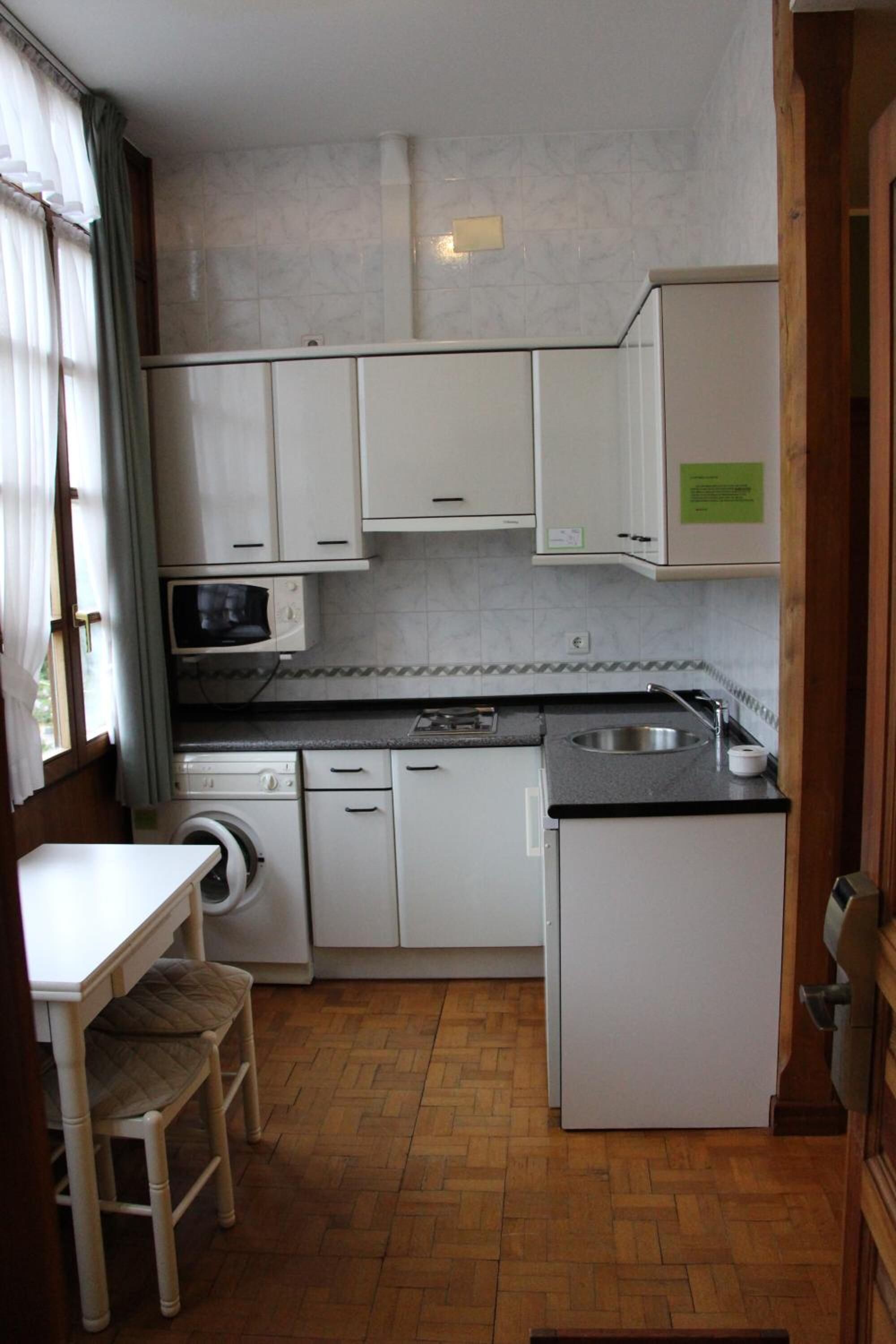 Una cocina compacta con armarios blancos, un microondas, un lavabo y una lavadora.