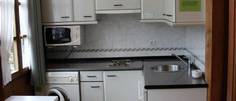 Una cocina compacta con armarios blancos, un microondas, un lavabo y una lavadora.