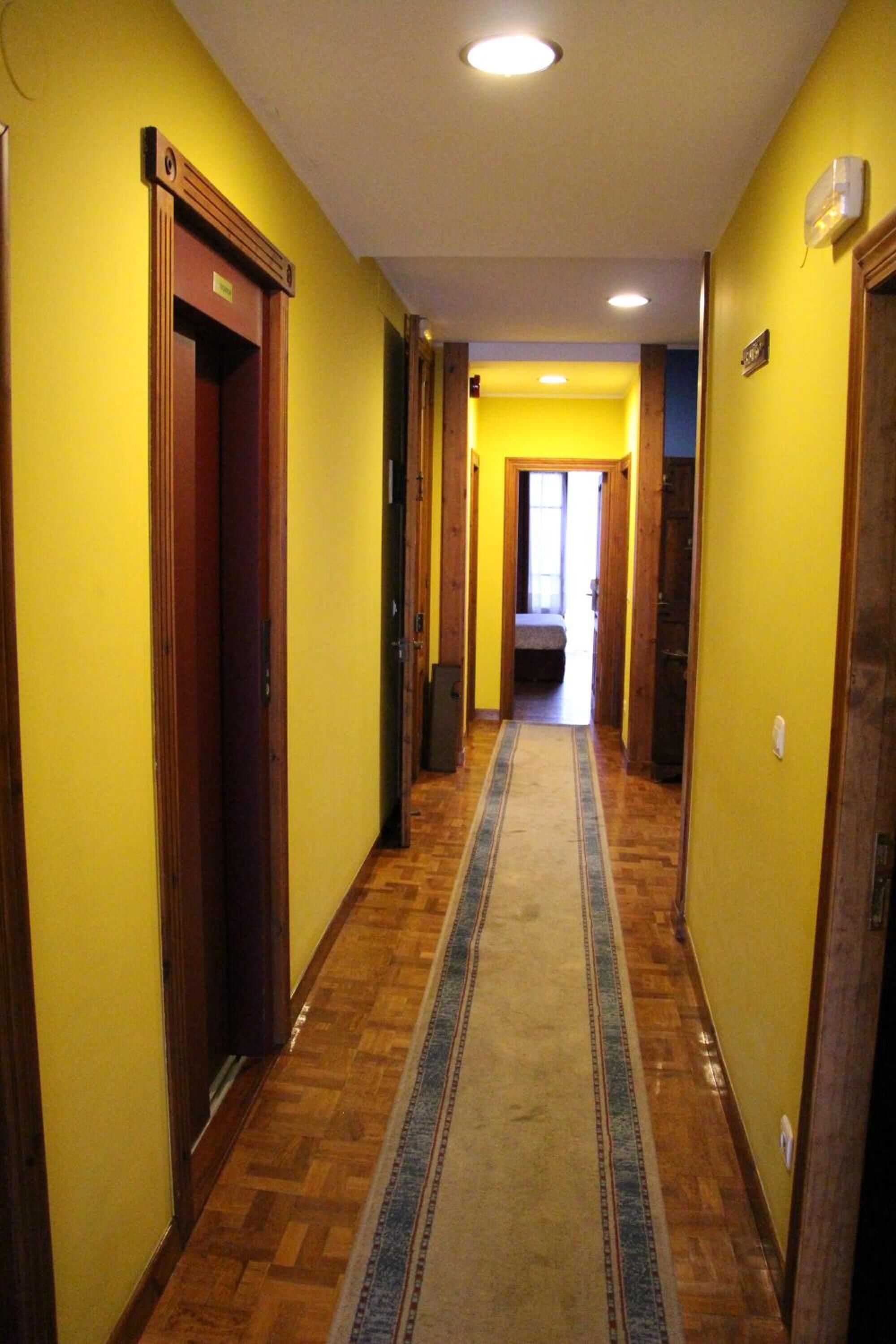 Un pasillo con pisos de madera, paredes amarillas y un tapete en el centro.
