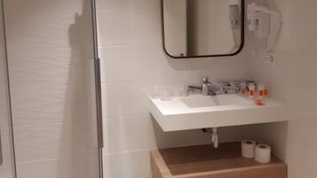 A modern bathroom with a glass shower enclosure, a white sink with a mirror above it, and a wooden shelf below.