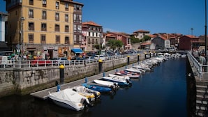 Un puerto deportivo con barcos amarrados a lo largo de un muro de piedra, rodeado de edificios de varios pisos con locales comerciales.
