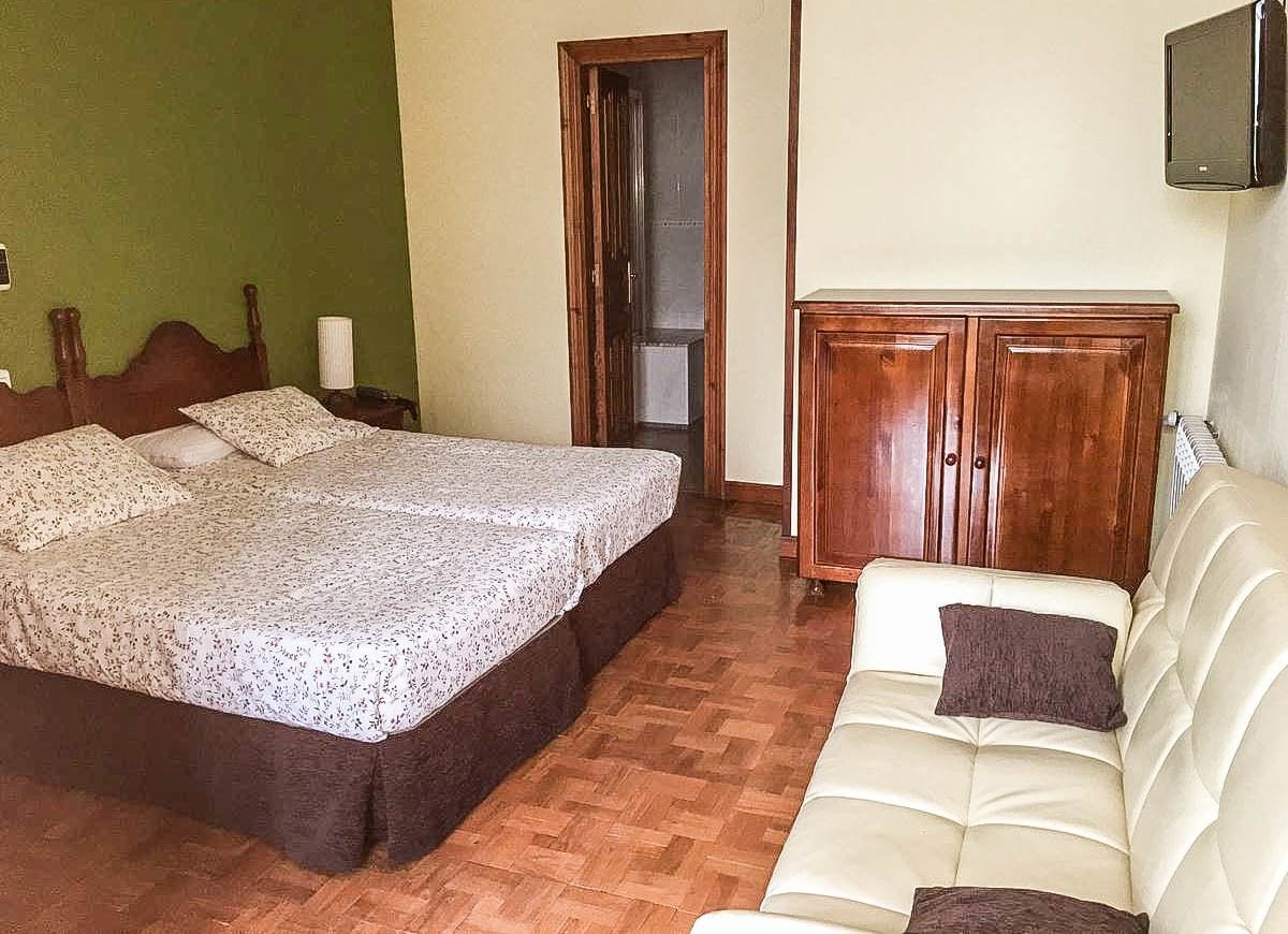 Een slaapkamer met een bed, een houten kledingkast, een bank en een televisie aan de muur.