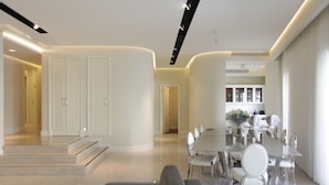 Een moderne woonkamer met een glazen eettafel, witte stoelen en een grijze bank.