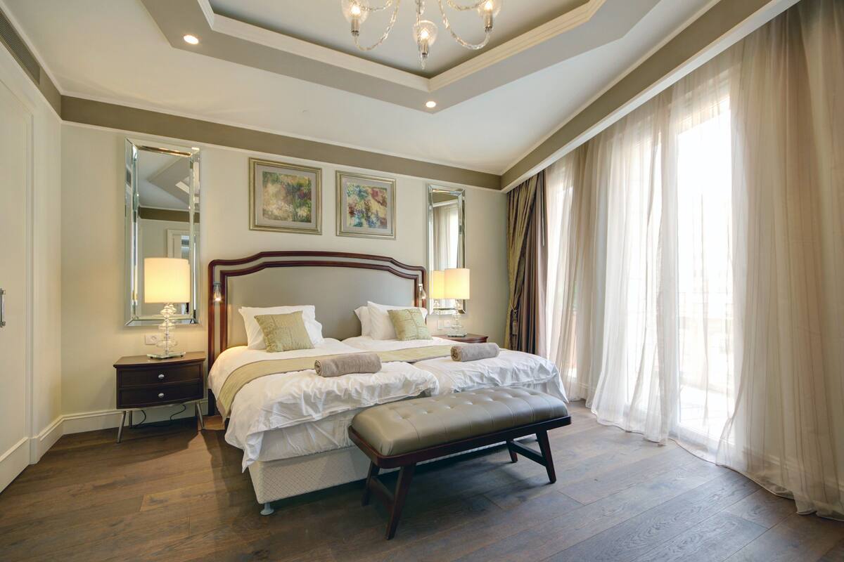 Une chambre spacieuse avec un grand lit, un banc et une table de chevet avec des lampes.