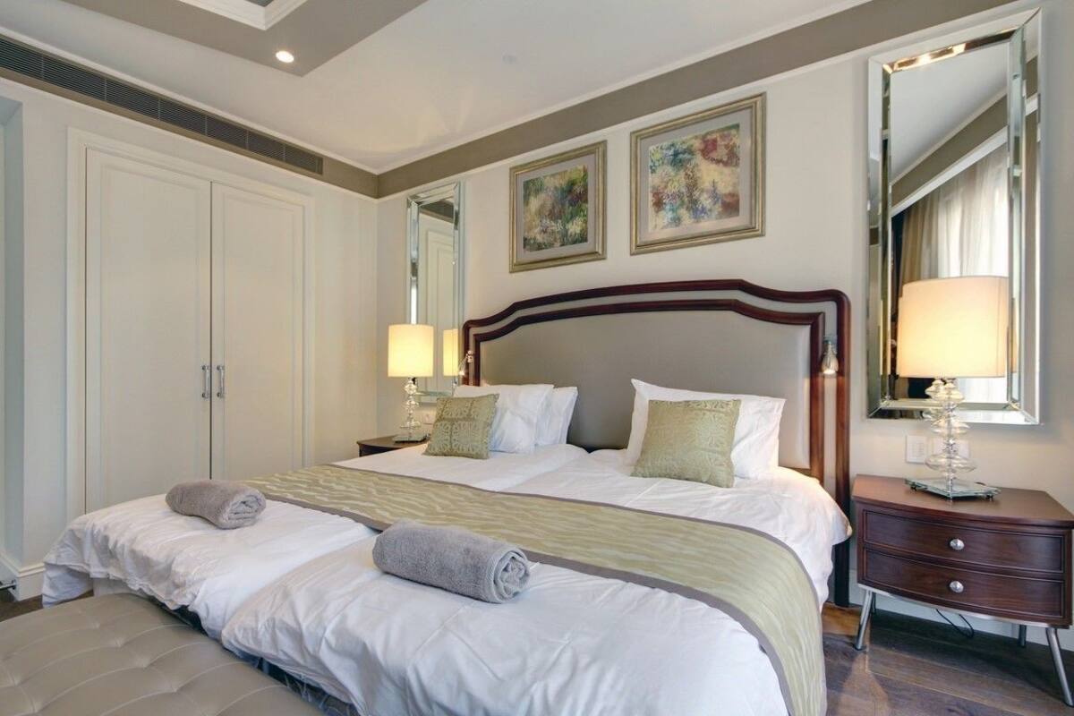 Une chambre d’hôtel élégamment aménagée, dotée d’un grand lit, de deux tables de chevet avec lampes, d’une armoire et d’œuvres d’art accrochées aux murs.