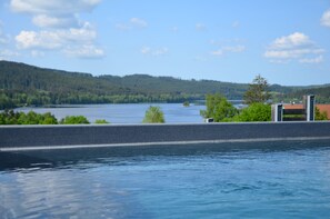 Ein See mit einer hölzernen Anlegestelle, die sich ins Wasser erstreckt, umgeben von Grünflächen und Hügeln.