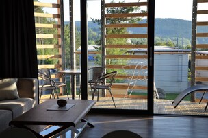 Una sala de estar moderna con un sofá, una mesa de comedor y vistas a una terraza exterior con sillas y una escalera.
