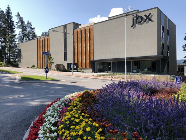 Ein modernes Gebäude mit einem 'jbx'-Schild, einem Parkplatzschild und einem Blumenbeet mit verschiedenen Blumen.