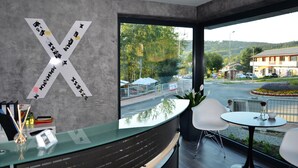 Een moderne hotel lobby met een grote 'X'-decoratie aan de muur, een receptiebalie en uitzicht op een straat met auto's en groen.