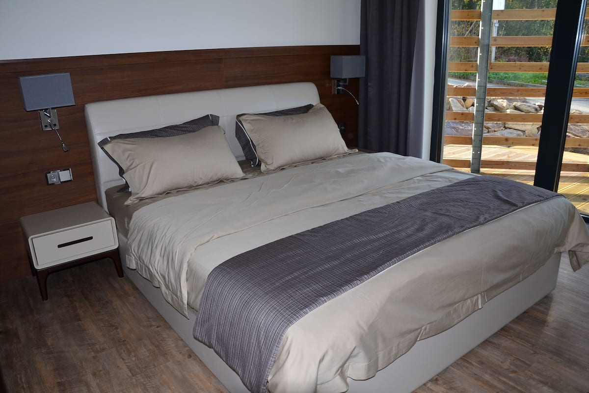 Un dormitorio moderno con una cama grande, mesitas de noche y vistas al exterior.