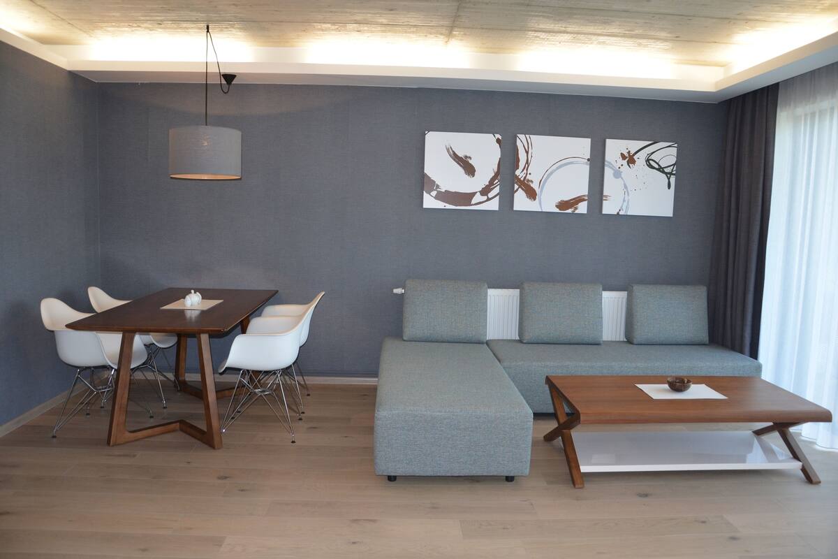 Una sala moderna con un sofá modular, una mesa de comedor con sillas y arte abstracto en la pared.